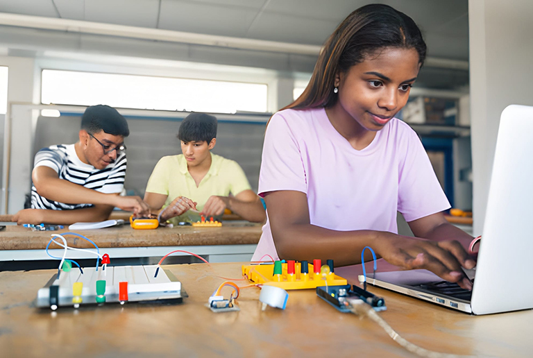 Young woman programming electronics on laptop during inclusive technology workshop.