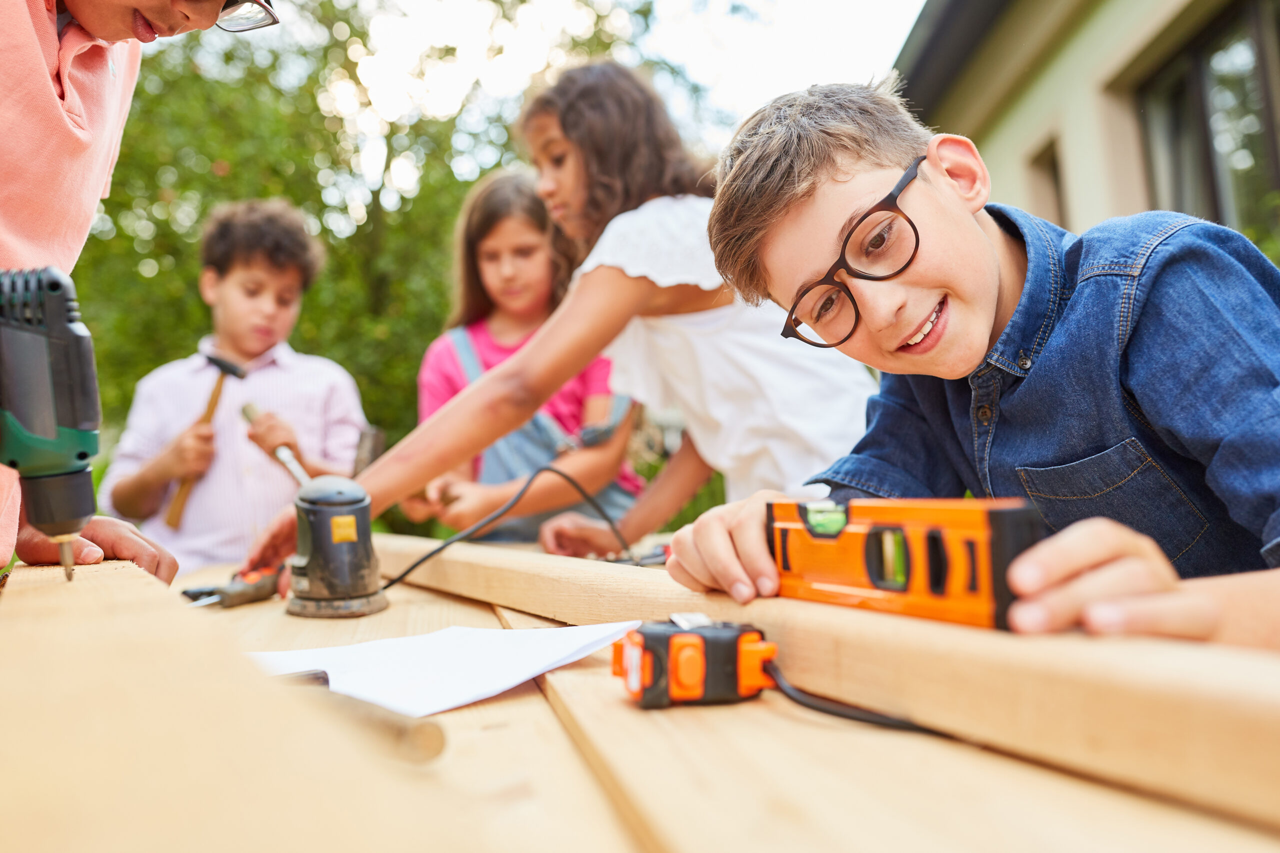 Children measuring and building a wooden project together outdoors