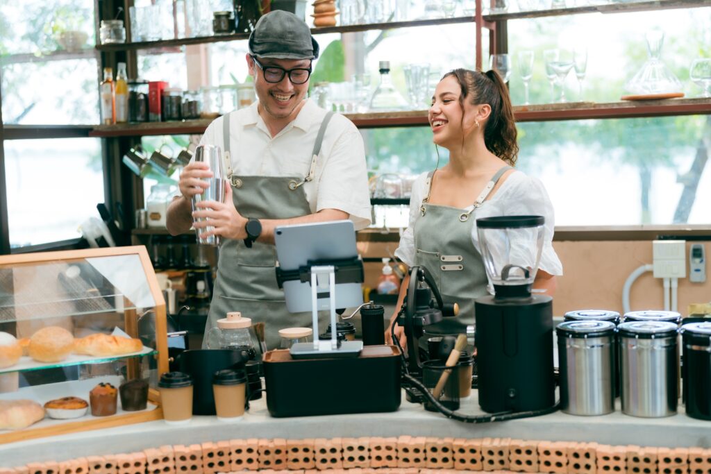 Two people smiling while preparing coffee at a café counter